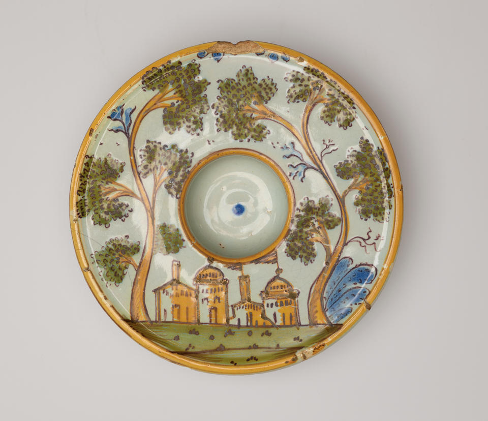 Round plate decorated with an image of buildings and trees. There is a concave well in the center of the form. 