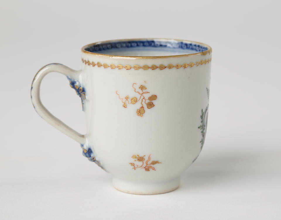 A porcelain chocolate cup with blue and gilded decorations along the outside and inside of the rim, body, and handle. 