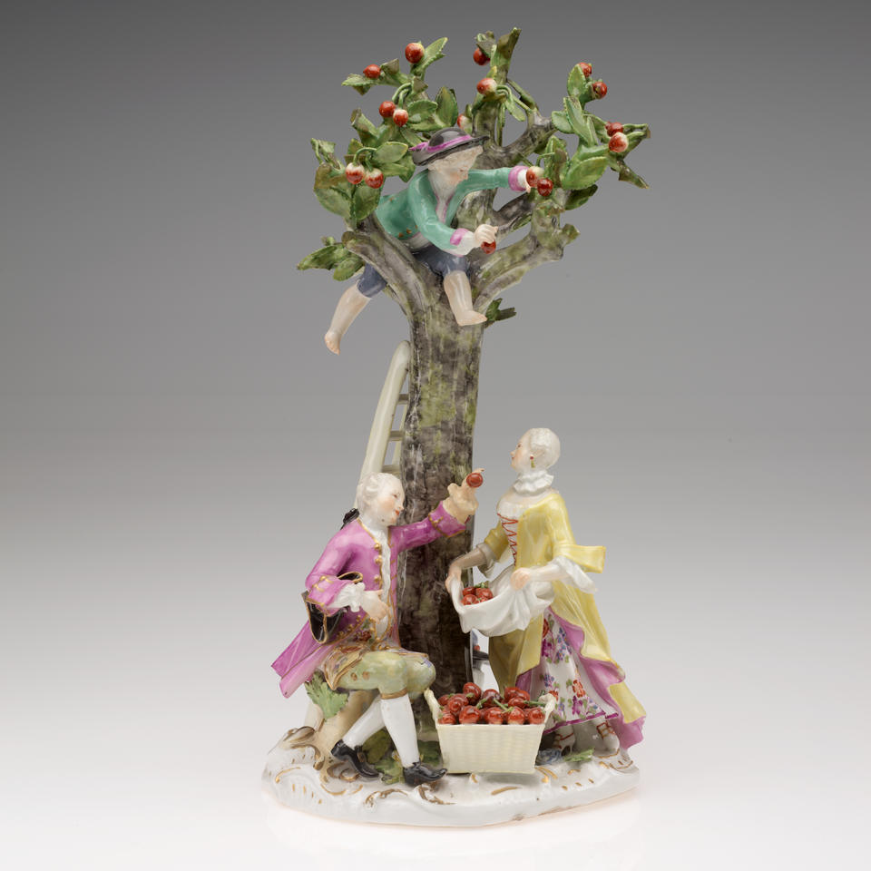 A sculpture with three figures in elaborate historical clothing (one in the tree, another sitting, and the last standing holding a basket), a cherry tree, a ladder and two baskets.