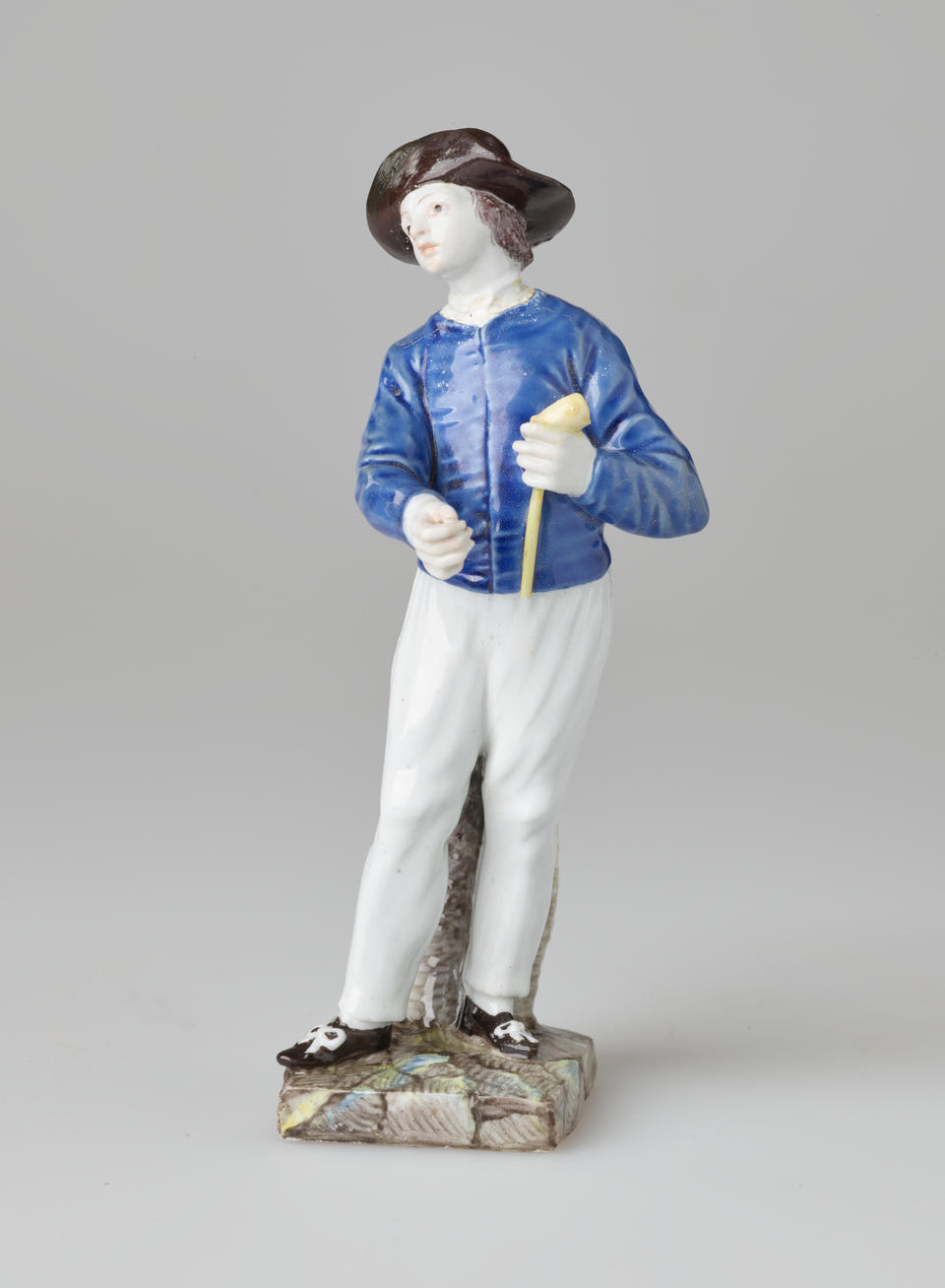 A sculpture of a figure in historical clothes, a blue shirt, white pants, black shoes and hat. The figure is also holding a pipe.