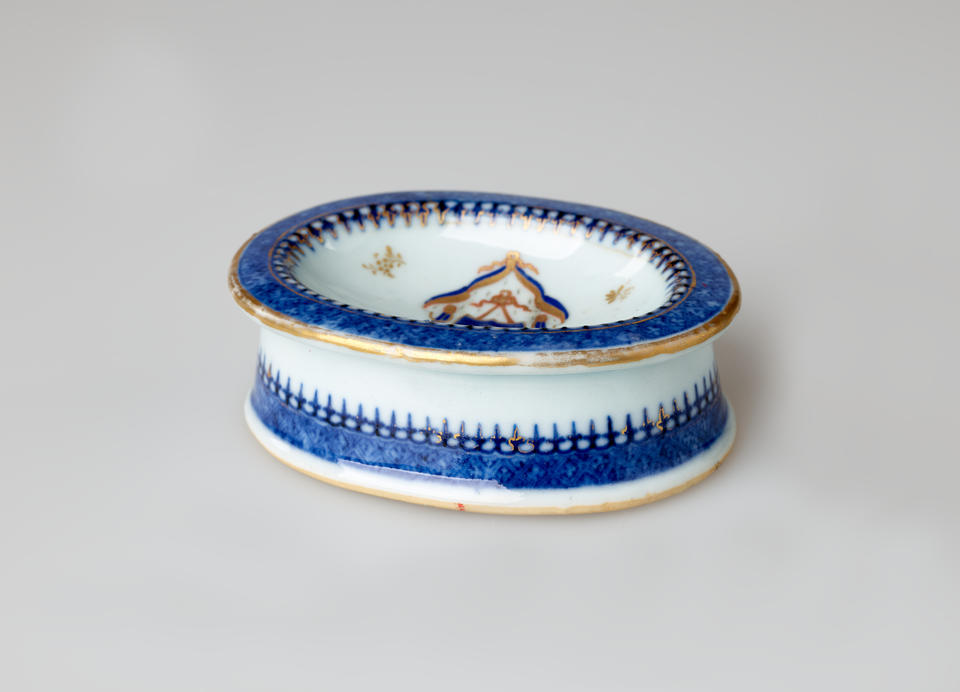 An oval porcelain white salt container with blue and gilded decorations. 