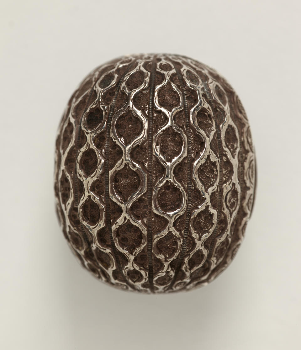 A silver nutmeg grater that is abstractly shaped like a nutmeg seed. 