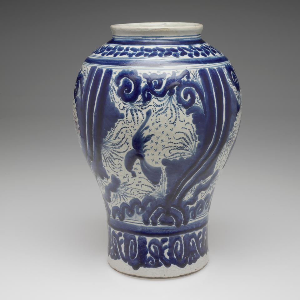 A vessel with a cylindrical bottom with a more bulbous top and a slightly flared out lip, it is glazed white and blue with abstract, purposeful and controlled decoration.
