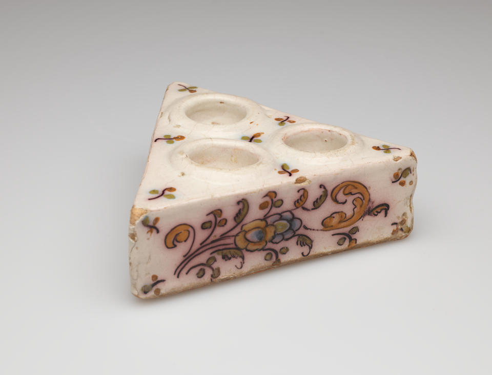 A cream colored triangular salt cellar with three holes on the top with decorative floral decorations.