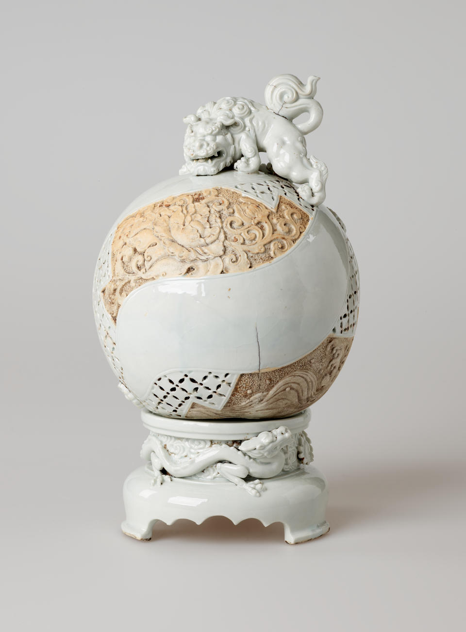 Light-colored sculptural globe with tan sections of ornate carving. An animal figure sits on top of the sphere. The base has a scalloped front edge and image of a dragon.