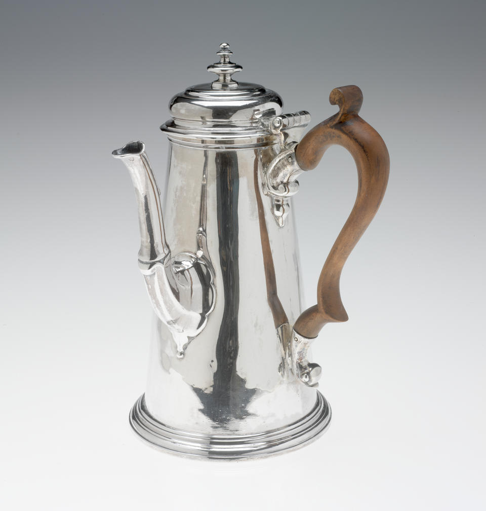 A silver chocolate pot with a spout, hinged lid, and fruitwood handle that is 90 degrees from the spout.