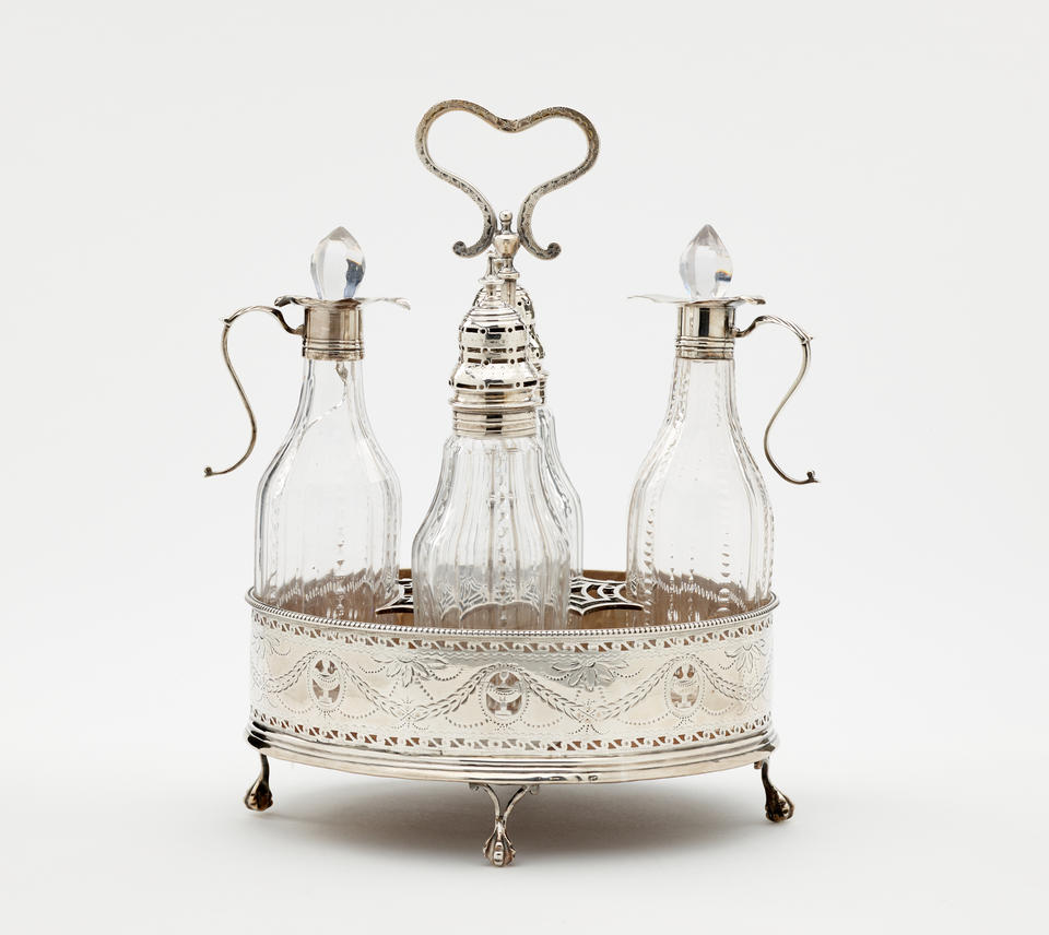 A silver, mahogany, and glass caster set. There are various vessels inside the footed tray. The silver and glass has etched decorations.