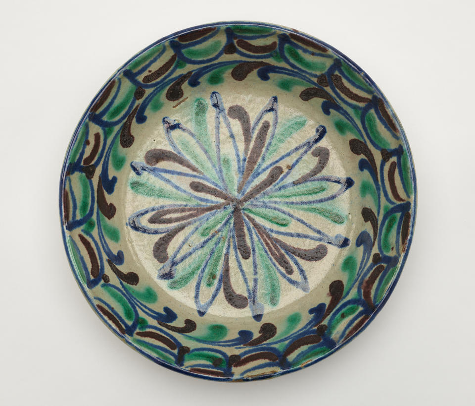 A gray-white circular cooking placate with blue, green, and gray symmetrical linear decorations.