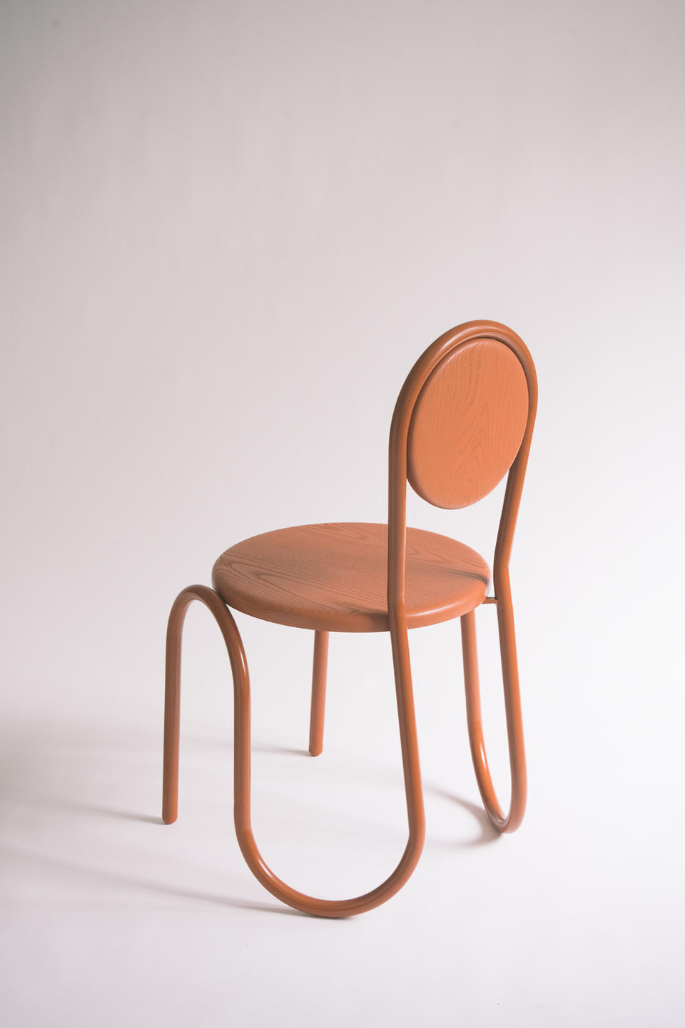 A brown wiggle steel tube chair frame with a wood circular seat and back.