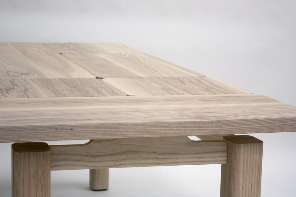 A wooden dining table with a puzzled rectangular top that appears to be floating over the substantial rectangular legs.