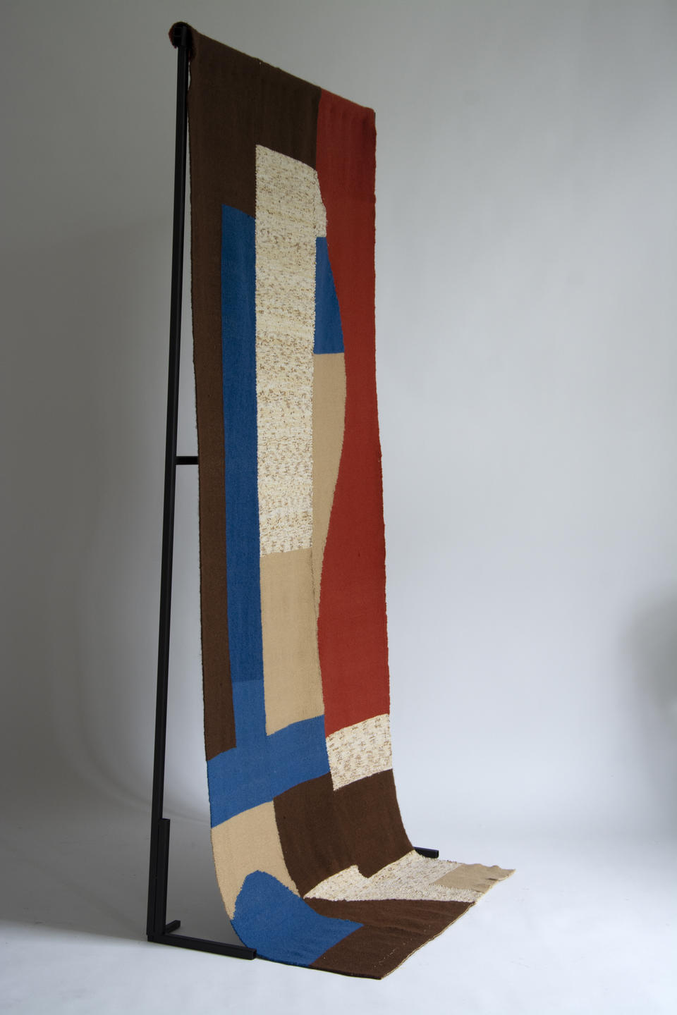 A woven tapestry, made of abstracted cobalt, vermillion, brown and beige shapes.