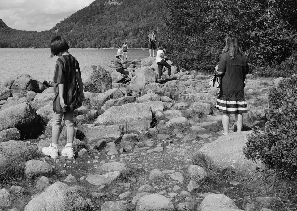 7 people standing in the shape of a triangle on top of boulders at the edge of a lake