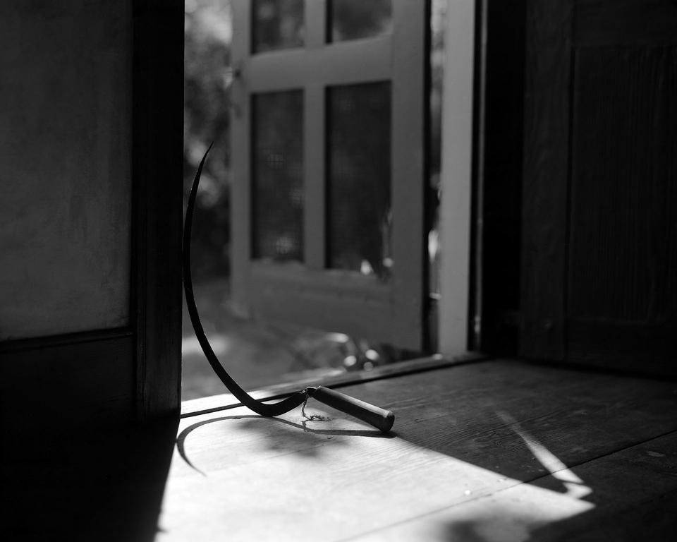 Grayscale photograph of a sickle inside of a door way. 