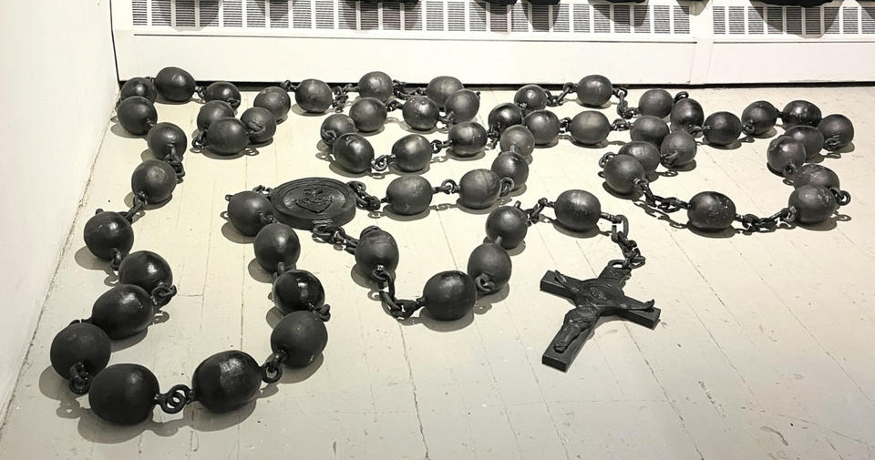The piece at is a gigantic rosary. And the beads are fashioned as the ball and chain seen in medieval prisons.