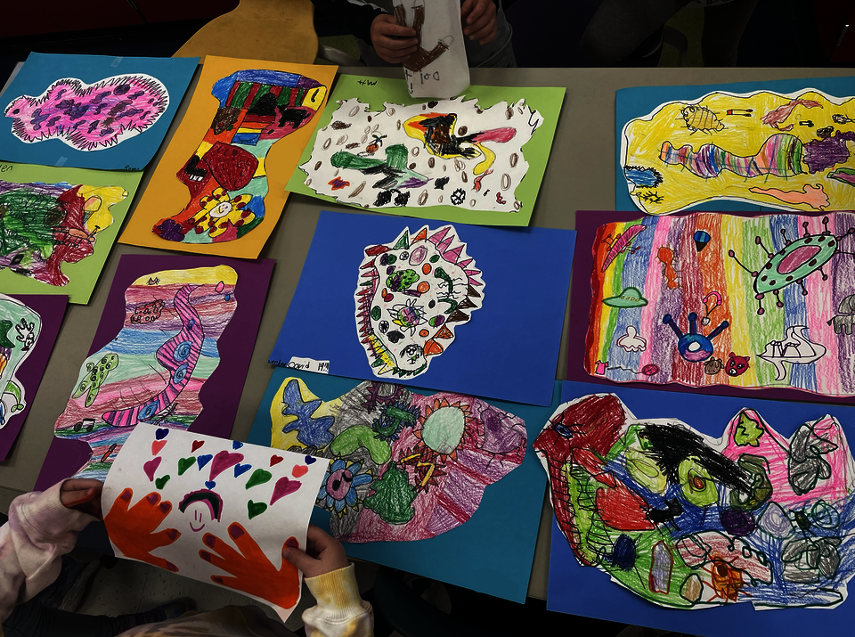A group of 1st graders art works laid out on a table.