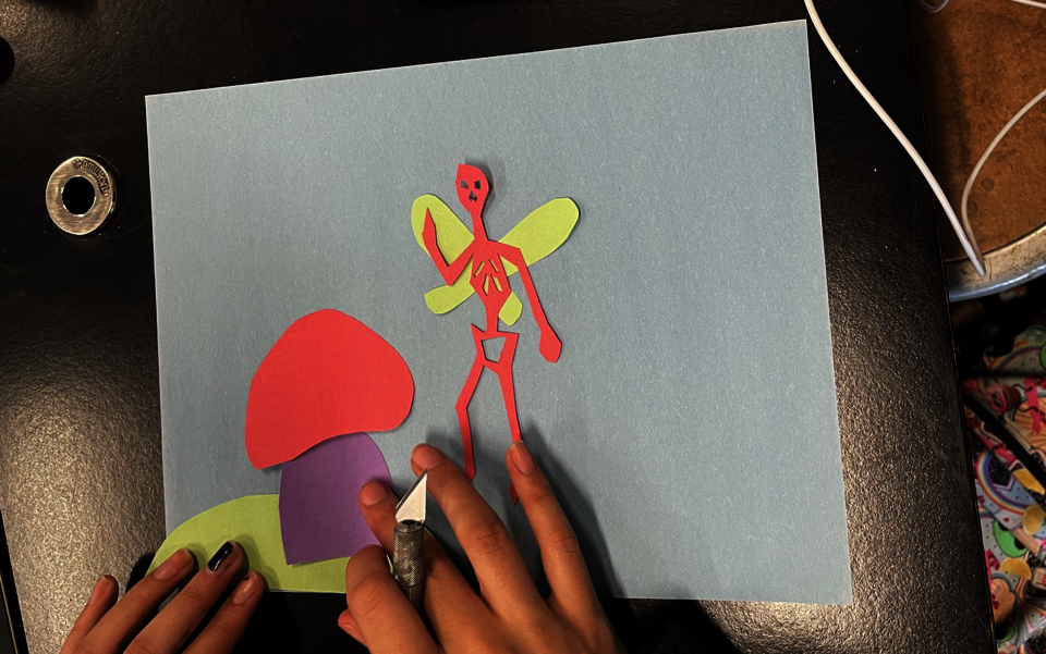 A student glues down her cut out shape onto a piece of construction paper. 