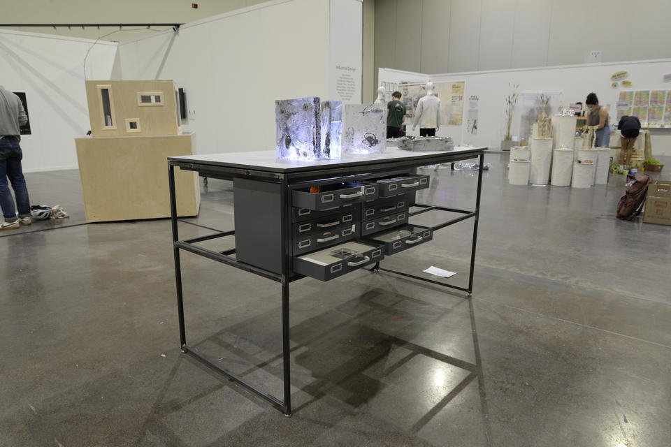 Thin metal standing-height desk with multiple drawers open. Glass books adorn the top of the table.