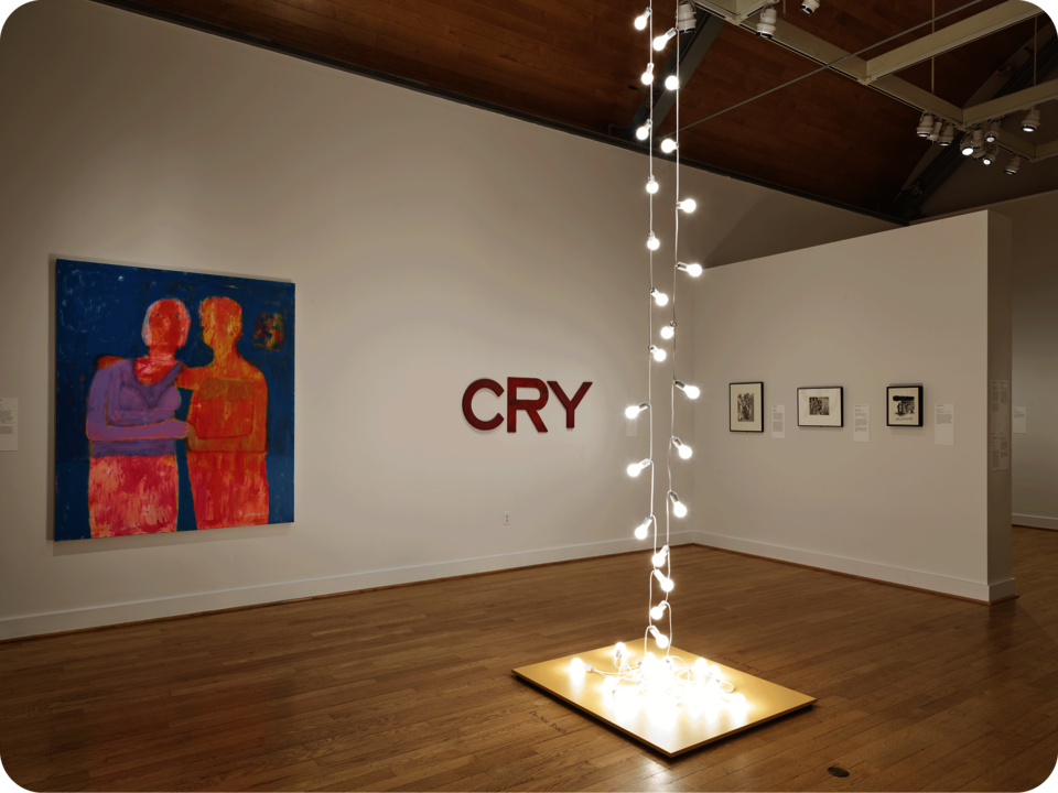 Installation view of an exhibit. Featured are a vibrant painting of two figures, an artwork spelling “CRY”, and monochromatic works. In the center space is a sculpture consisting of lightbulbs. 