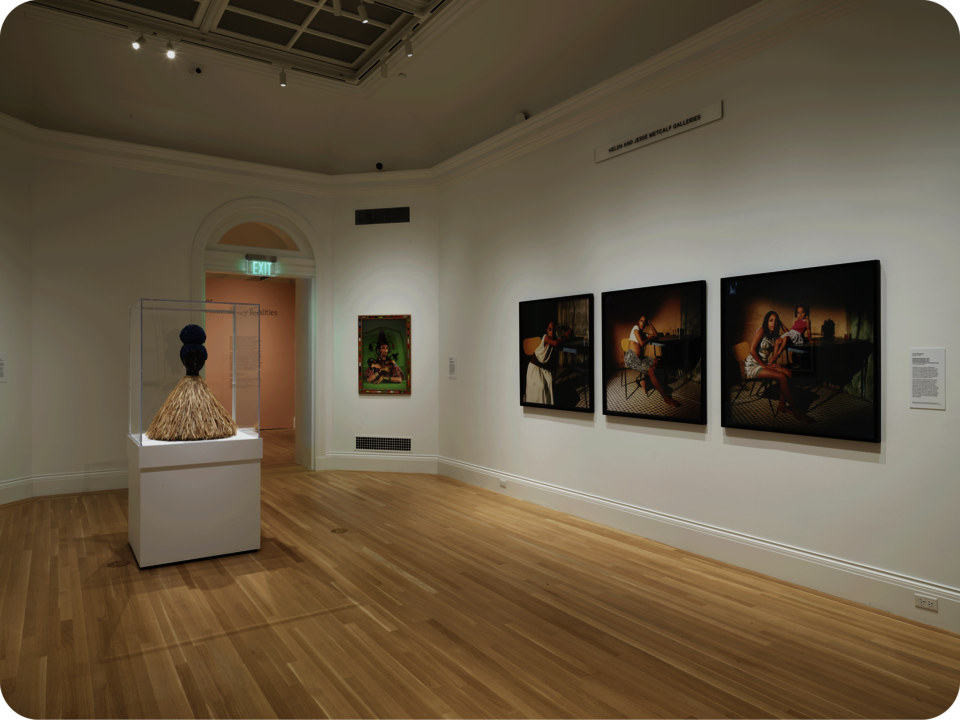 Exhibition documentation. 3 photographs in a similar style are hung on one wall, with another photo on the adjacent wall. A bust in a glass case occupies the space’s center.