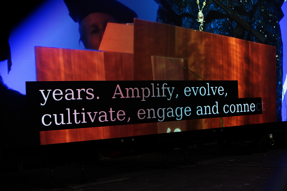 Photo of a projection of a podium, with the caption 'years. Amplify, evolve, cultivate, engage and come.'