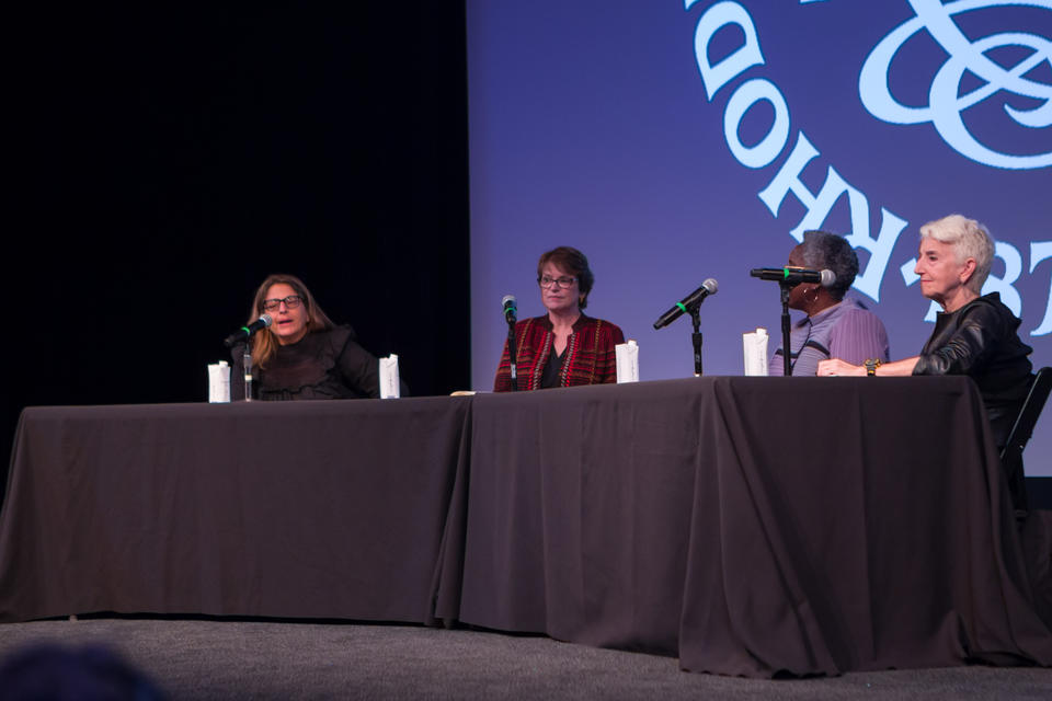 Close-up shot of four women panelists on stage at a table draped in a black cloth.