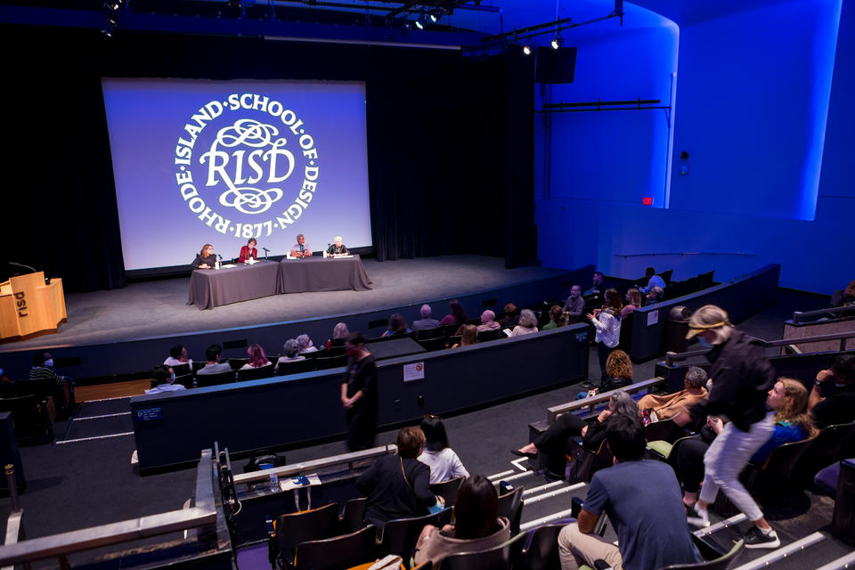 A panel of four people presents in an auditorium. The RISD seal is projected behind them.