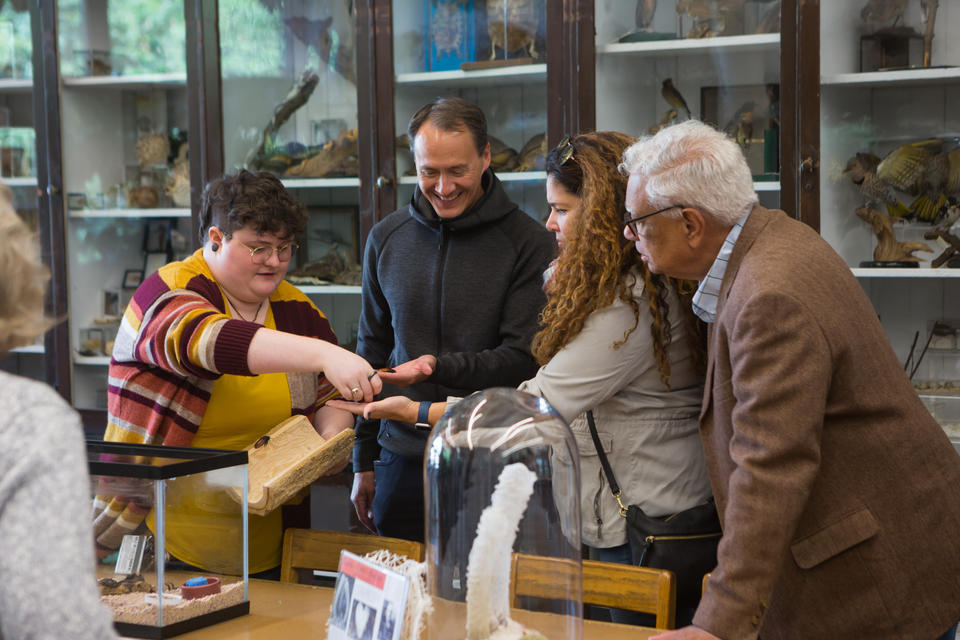 A student holding a half log hands out Madagascar hissing cockroaches to three smiling adults.