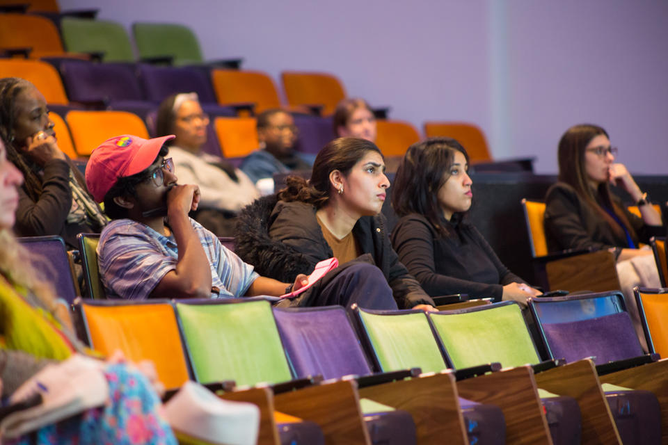 Interested observers sit and ponder in colorful auditorium chairs.