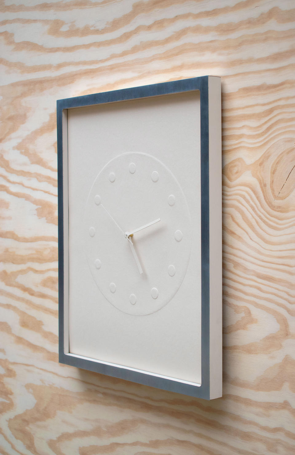 A clock made of embossed paper and presented in a custom frame.