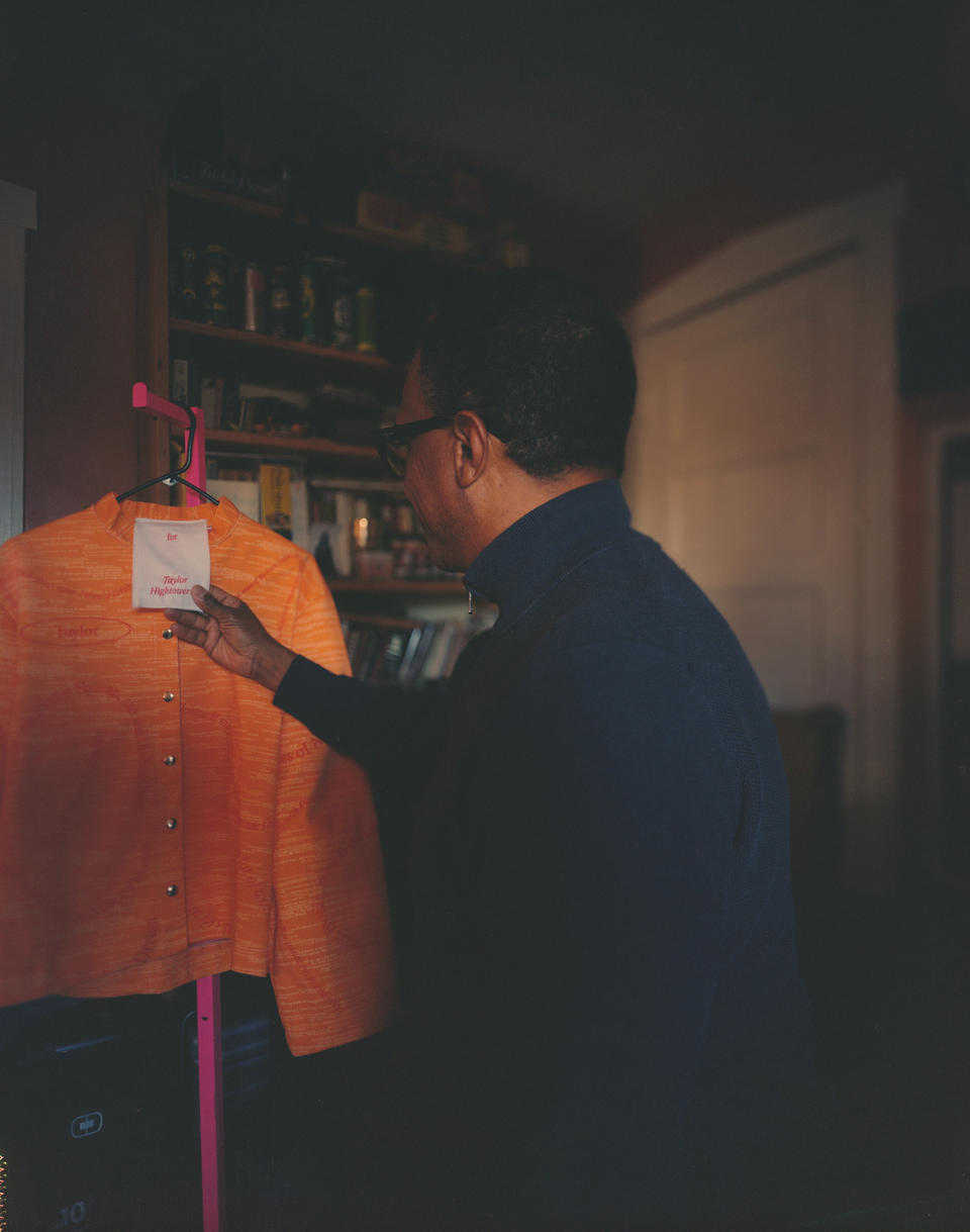 Man in the right-hand side of the frame looking over his shoulder at an orange jacket hanging from a clothing rack.