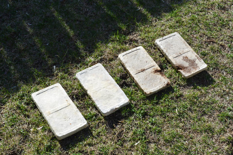 Four whitish-brown bricks laid in grass, deteriorating in color and form from right to left