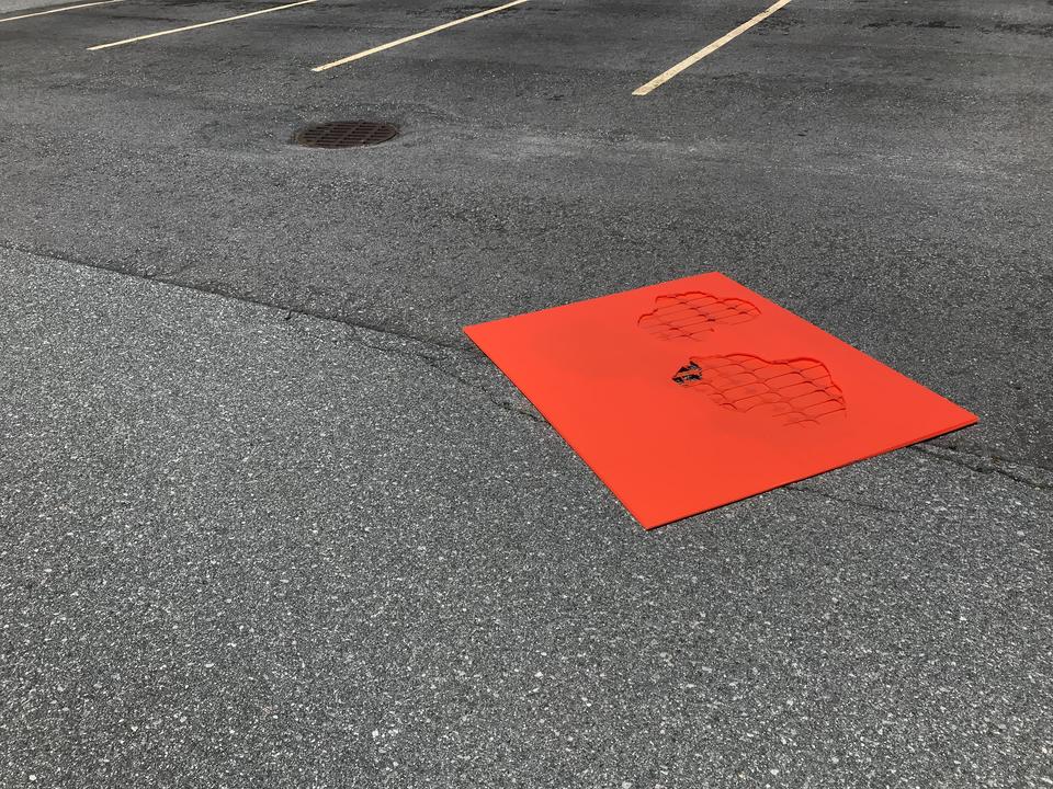 A flat orange plastic rectangle with cut-outs lays on the asphalt of an empty parking lot.