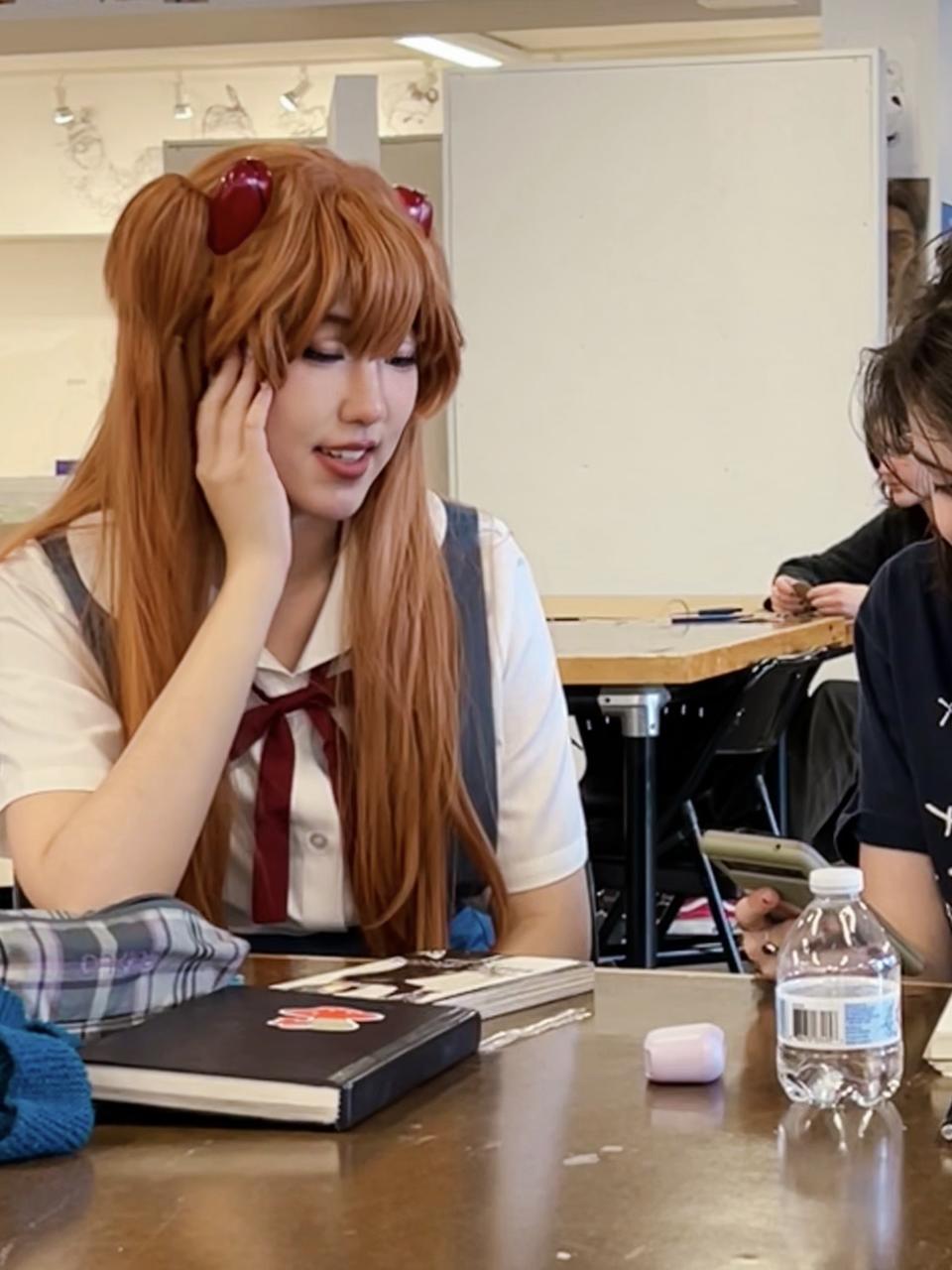 The author dressed as Asuka Langley Soryu, a female fictional character from the Japanese franchise Neon Genesis Evangelion, discussing development plans with a student.