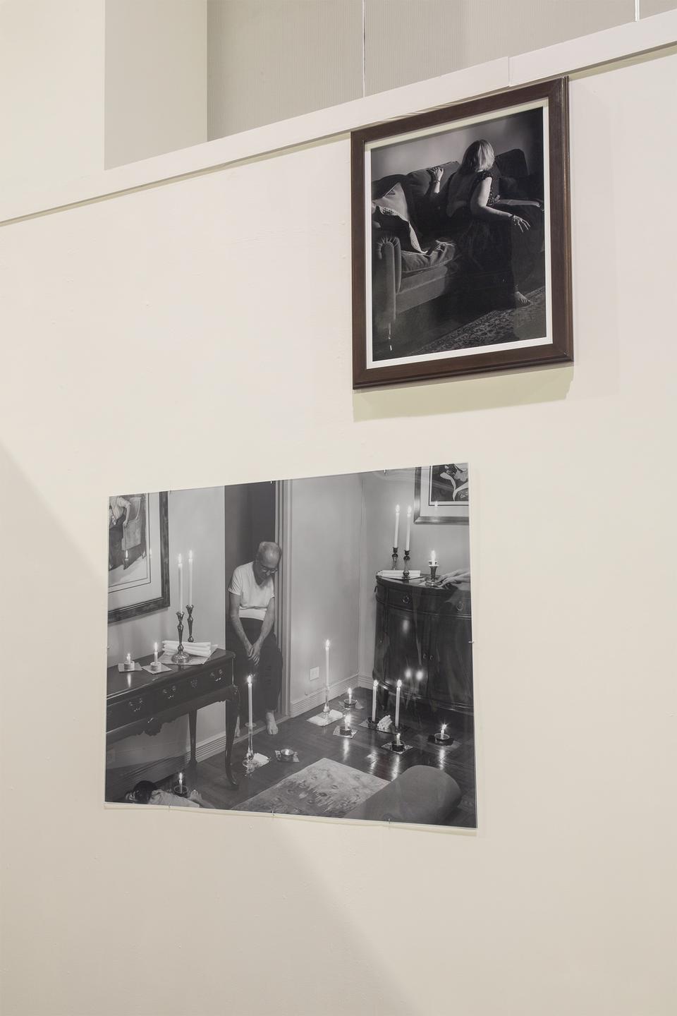 Framed black and white photograph of woman on a couch with an undone dress above a photograph of a living room candle arrangement mounted behind plexiglass.