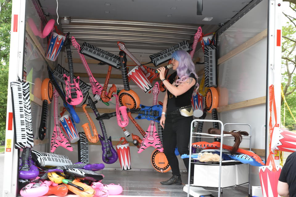 Person performing Restaurant Menu karaoke in the back of Uhaul Truck with decorated with inflatable instruments. 