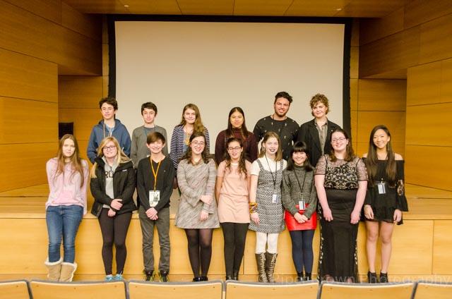 Image for sixteen young people in two rows standing in the theater with a film screen behind them. 