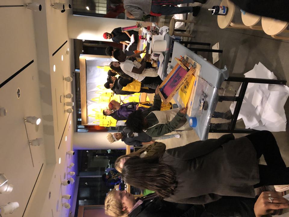 Crowd of teenagers in front of tables with screenprinting stations 