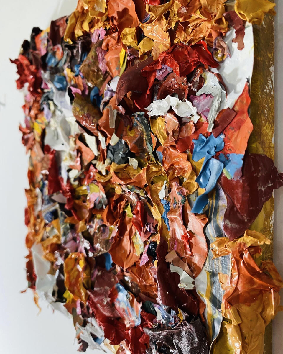 Small pieces of scrap paint are glued onto a canvas. The pieces vary but are roughly 1"x1". The scrap colors are red, yellow, blue, orange and white.