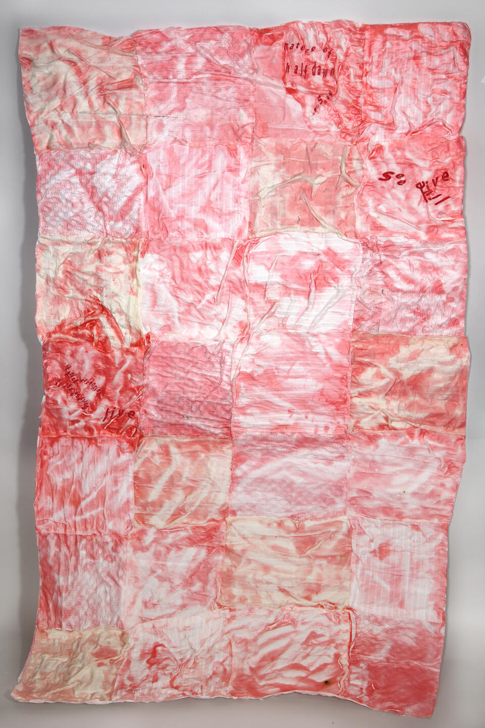 a cotton quilt with a red, plastic film and embroidered text over it reading " Nature of Half Dawn."