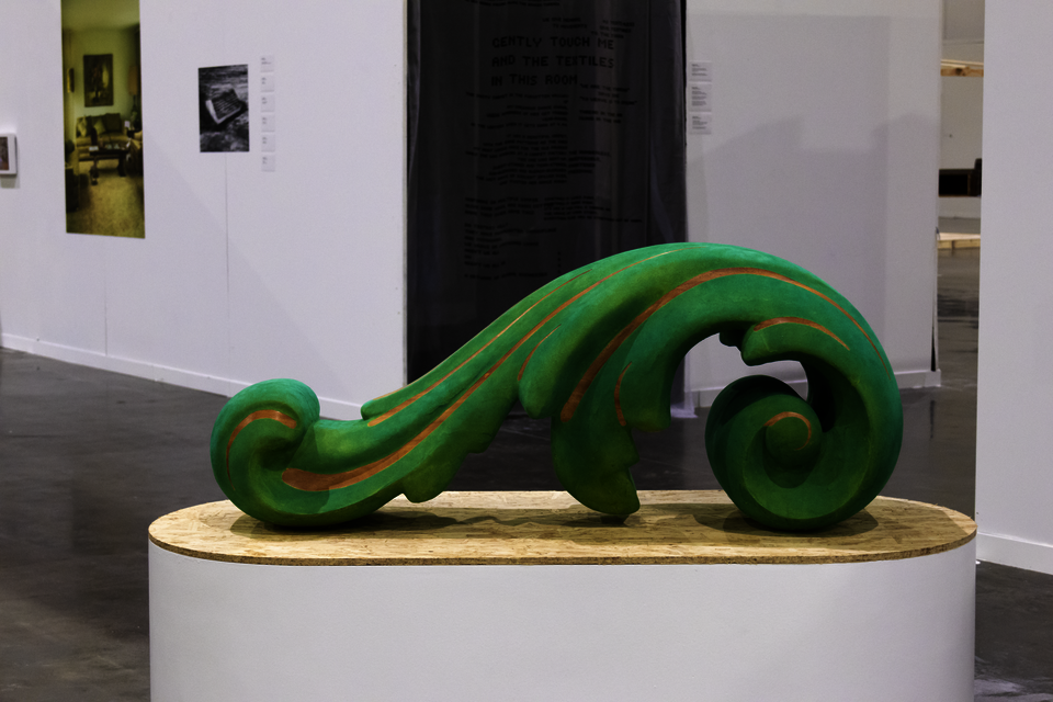 A large green acanthus ornament sits on a high pill-shaped plinth with an Oriented Strand Board top surface.