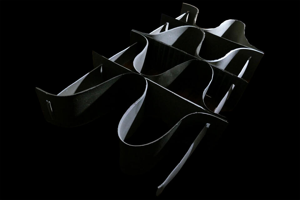 A shelf composed of seven thin, curved, ribbon-like forms intertwined and overlapping against a black background. The oyster biomaterial Shellf Life has a reflective, silver-toned surface that catches the light for a beautiful furniture design.