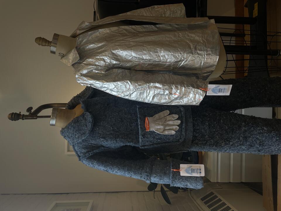Two jackets, one made from recycled denim insulation, the other from silver Tyvek, on two mannequins with garment tags that say "Waste Coats"