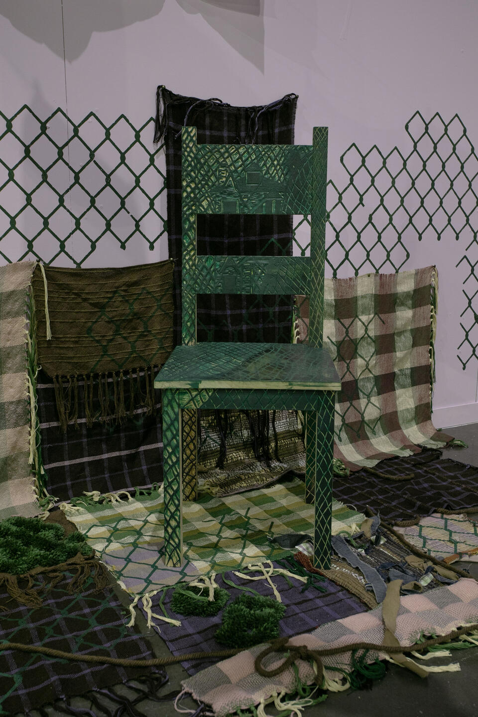 image of carved green chair standing on top of woven fabrics travelling from the wall to the floor with chainlink motif printed on top with purple background