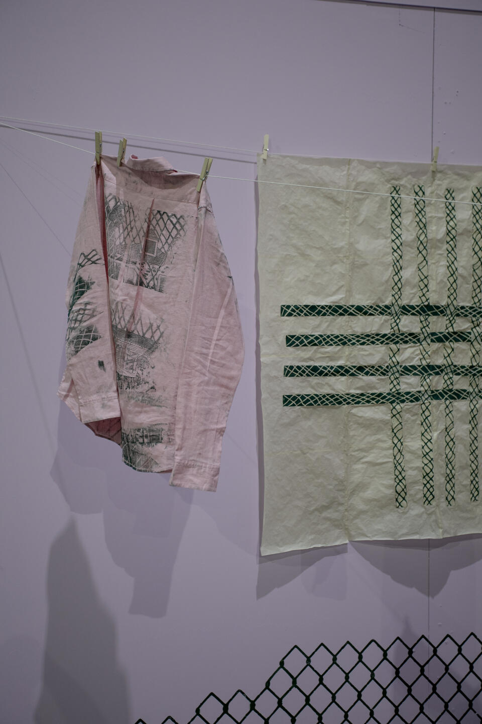 pink shirt with green woodcut prints depicting a house and intersecting lines 