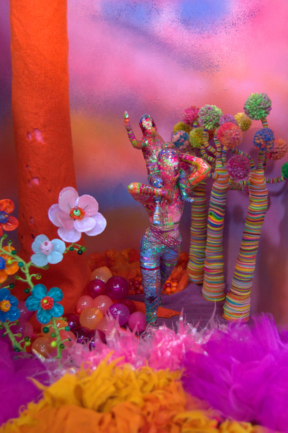 A colorful, glittering child sits atop the shoulders of a similarly colored adult as they walk through a fantasy forest with striped wool trees and large glass flowers