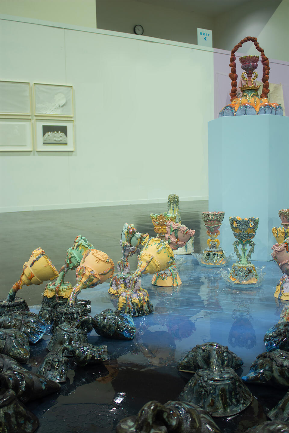 Colorful ceramic vessels arranged in clusters on a reflective surface, with a central pedestal holding an elaborate piece. The holy grails are gradually changing colors.   