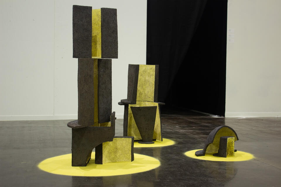 A collection of textured, geometric ceramic sculptures in various shapes, predominantly yellow with black accents, displayed on yellow circular bases.