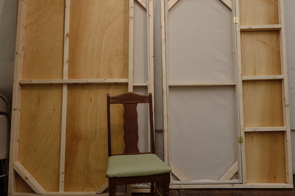Image of deconstructed walls that make up the thesis booth - made of wood and cloth, with a wooden chair in front