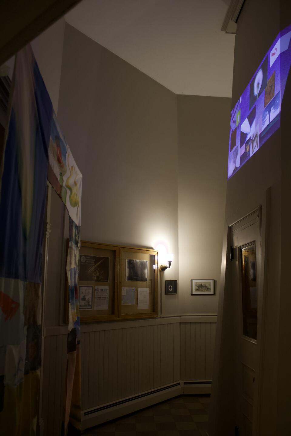An image of a darkened interior space, a doorway covered in fabric and an animation with multiple moving windows projected on opposite wall