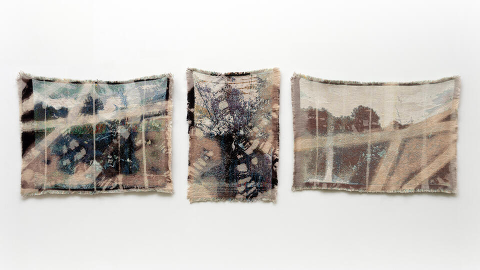 Three Small Scale weavings depicting blurry landscapes hanging in a horizontal row.
